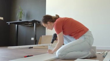 Beyaz yatak çerçevesine vidalamak için kablosuz matkap kullanan kadın. Yeni dairede mobilya montajı yapan bir kadın. DIY ev yenileme ve taşınma konseptinden sonra ev organizasyonu