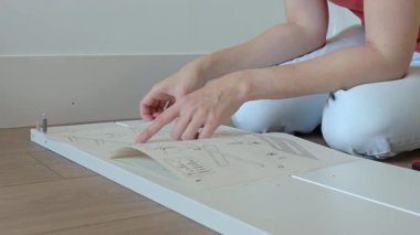 Mobilya montajı sırasında yerde oturmuş kullanma kılavuzunu okuyan bir kadın. Yerde aletlerin ve yeni yatağın parçalarının yanında oturan biri. DIY ev geliştirme ve mobilya kurulumu kavramı