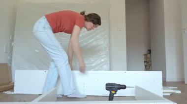 Yeni evde mobilya montajı yapan bir kadın, beyaz yatak çerçevesinin parçalarını bağlıyor. DIY ev yenileme ve taşınma konseptinden sonra ev organizasyonu