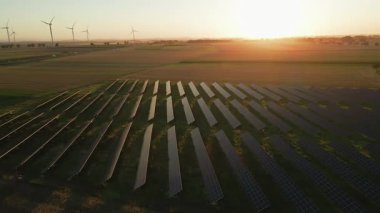 Güneş panelleri ve kırsal alanda güneş batarken rüzgar türbinleri. Yenilenebilir enerji kavramı, sürdürülebilir teknoloji ve temiz elektrik üretimi