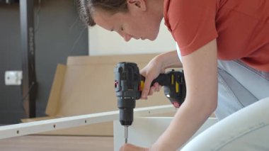 Beyaz yatak çerçevesine vidalamak için kablosuz matkap kullanan kadın. Yeni dairede mobilya montajı yapan bir kadın. DIY ev yenileme ve taşınma konseptinden sonra ev organizasyonu