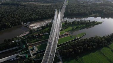 Geniş nehir üzerinde yeşil tarlalar ve ormanlarla çevrili baraj ve kilit sistemi olan kablo manzaralı köprü.