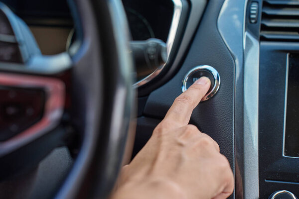 Close-up of hand pressing start button to turn on car engine. Keyless ignition system in modern car