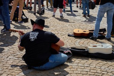 Wroclaw 'daki Guitar World Record etkinliği sırasında gitarların arasında gitar çalan siyah şapkalı ve tişörtlü bir adam. Wroclaw, Polonya - 1 Mayıs 2025