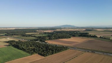Tarımsal tarlaların yakınındaki kamyon ve arabalarla otoyol manzarası ve arka planda dağlar olan ormanlar