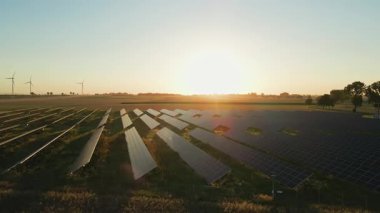 Güneş panelleri ve kırsal alanda güneş batarken rüzgar türbinleri. Yenilenebilir enerji kavramı, sürdürülebilir teknoloji ve temiz elektrik üretimi