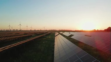 Güneş panelleri ve kırsal alanda güneş batarken rüzgar türbinleri. Yenilenebilir enerji kavramı, sürdürülebilir teknoloji ve temiz elektrik üretimi