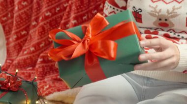 Yeşil Noel hediye paketini kırmızı kurdeleyle tutan ellerinizi kapatın. Bayram kutlaması ve hediye verme kavramı