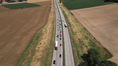Tek şeritte trafik sıkışıklığı olan yeşil tarlalarla çevrili otoyolda giden arabaların hava görüntüsü. Ulaşım, trafik ve altyapı kavramı