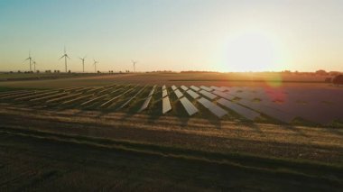 Güneş panelleri ve kırsal alanda güneş batarken rüzgar türbinleri. Yenilenebilir enerji kavramı, sürdürülebilir teknoloji ve temiz elektrik üretimi