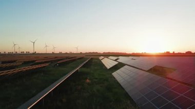 Güneş panelleri ve kırsal alanda güneş batarken rüzgar türbinleri. Yenilenebilir enerji kavramı, sürdürülebilir teknoloji ve temiz elektrik üretimi