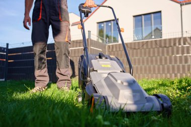 Arka bahçede çim biçmek için elektrikli çim biçme makinesi kullanan biri. Banliyö evinin yakınında çim biçen bir adam. Bahçe bakımı, bahçe bakımı ve açık hava işi kavramı