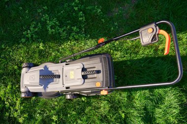 Bahçedeki yeşil çimlerin üzerinde elektrikli çim biçme makinesinin manzarası. Bahçe bakımı, bahçe düzenlemesi ve banliyö ev bakımı kavramı