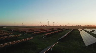 Güneş panelleri ve kırsal alanda güneş batarken rüzgar türbinleri. Yenilenebilir enerji kavramı, sürdürülebilir teknoloji ve temiz elektrik üretimi