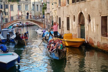 Venedik, İtalya 'da gondolcu ve turistlerin gezdiği geleneksel gondollar. Diğer tekneler ve arka plandaki köprüde duran insanlar. Venedik, İtalya - 26 Ağustos 2025