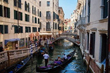 Venedik, İtalya 'da gondolcu ve turistlerin gezdiği geleneksel gondollar. Diğer tekneler ve arka plandaki köprüde duran insanlar. Venedik, İtalya - 26 Ağustos 2025