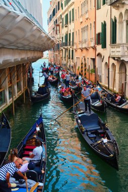 Venedik, İtalya 'da gondolcu ve turistlerin gezdiği geleneksel gondollar. Diğer tekneler ve arka plandaki köprüde duran insanlar. Venedik, İtalya - 26 Ağustos 2025