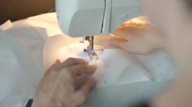 Elbise dikmek için dikiş makinesi kullanan bir kadın. Kadın ellerini kapat, dikiş makinesi iğnesi yap ve iplikle ayağını bastır.