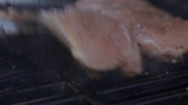 Arka bahçede ızgarada metal maşayla çevirilmiş ızgara et bifteği yakın.