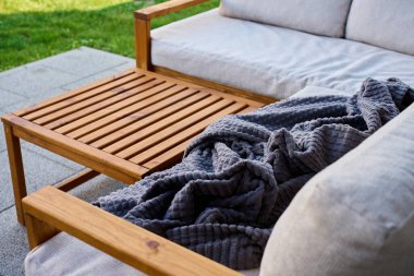 Açık köşedeki kanepe, hafif yastıklar, ahşap masa ve fayanslı terasta gri battaniye. Rahatlama, avlu konforu ve modern açık hava yaşam tarzı kavramı