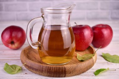 Apple juice in a transparent decanter and red apples on a wooden tray.