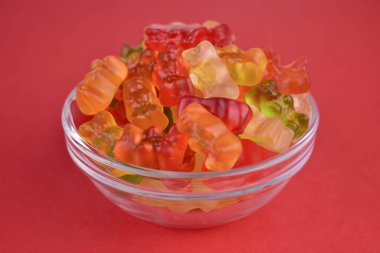 Many multi-colored jelly bears in a plate on a red background. Close-up.