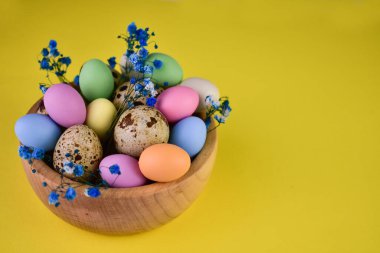Easter painted eggs in a wooden bowl on a yellow background.