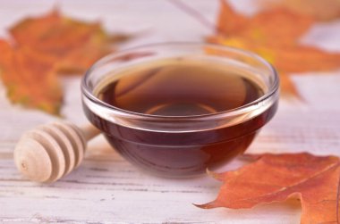 Akçaağaç şurubu beyaz ahşap bir arka planda cam bir kasede. Yakın plan..