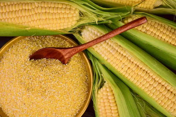 Corn grits in a bowl against a background of fresh corn on the cob. The concept of producing cereals from grains, corn products.
