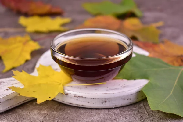 Maple syrup in a small glass bowl against a background of autumn maple leaves.