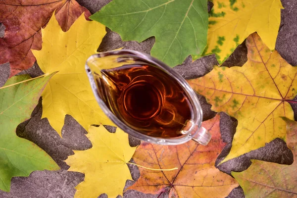 Maple syrup in a glass decanter against a background of autumn maple leaves. Flat lei.