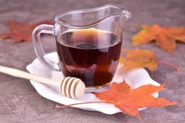 Gri bir arka planda şeffaf bir sos teknesinde tatlı akçaağaç şurubu.