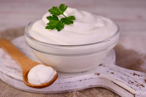 Сметана в стеклянной миске с кусочком петрушки.