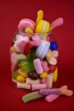 Kırmızı arka planda bir kavanozda bir sürü farklı şeker..