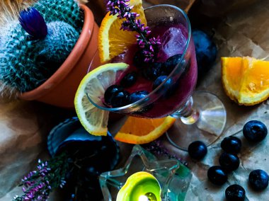 Arka planda meyve ve kaktüsle çevrili buzlu Blackberry alkol içeceği.