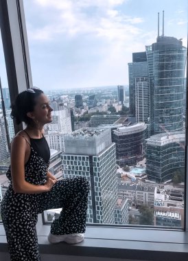 Genç ve güzel bir kadının portresi. Binanın tepesinde. Pencere ve şehir manzarasına bakıyor.