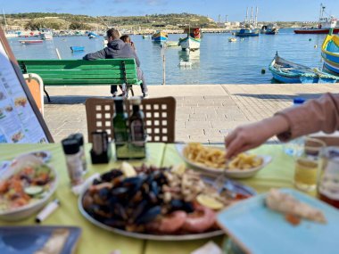 Marsaxlokk, Malta 'da bir masanın önünde oturan kimliği belirsiz insanlar..