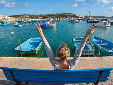 Marsaxlokk limanında bankta oturan ve teknelere bakan bir kadın, Malta