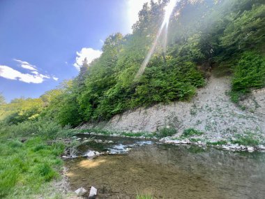 Nehre bitişik sarp kayalıklar güzel yeşillikler ve ağaçların arasında.