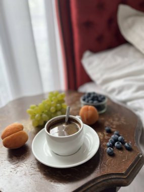 Yatakta kahvaltı. Otel odasındaki ahşap masada taze meyveli bir fincan kahve..