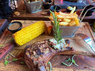 Patates kızartmalı ızgara biftek, ahşap masada mısır ve sos.