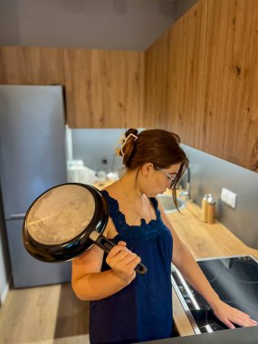 Mutfakta elektrikli ocağın yanında genç bir kız elinde bir tava tutuyor ve aletleri anlamaya çalışıyor.