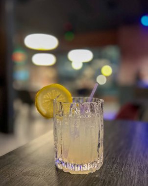 Arkaplanı bulanık, ahşap bir masada limonlu ve buzlu alkol kokteyli.