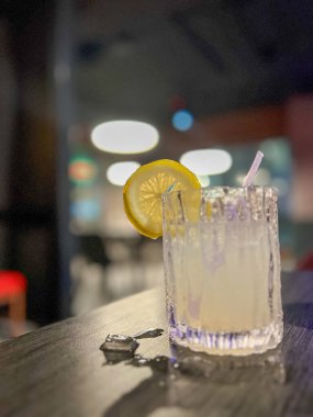 Arkaplanı bulanık, ahşap bir masada limonlu ve buzlu alkol kokteyli.