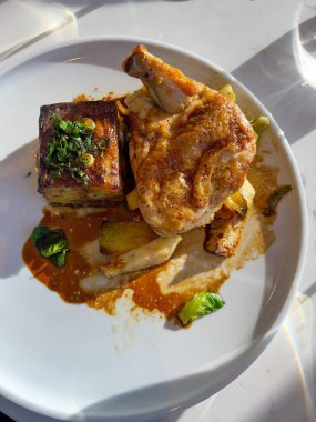 Restorandaki beyaz tabakta patates ve otla ızgara tavuk budu.