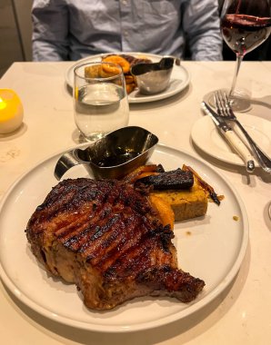 Beyaz bir tabakta ızgara biftek ve bir bardak kırmızı şarap.