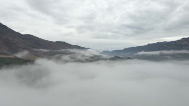 Sabahın erken saatlerinde bulutların arasından yüksek karlı dağlara doğru uç.
