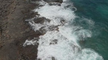 Dalgalar kayalık kıyıya çarpıyor. Drone görüntüsü, yavaş çekim. Kayalık kıyı ve dalgalar üzerinde uçmak. Okyanus kıyısı