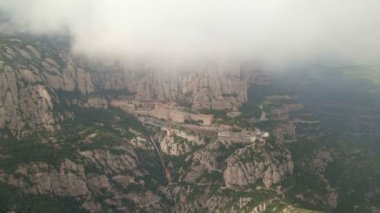 Montserrat Manastırı. İHA görüntüsü. İnsansız hava aracı bulutların altından manastıra doğru uçuyor. Görkemli hava yolculuğu: bulutlardan yükselen Montserrat Manastırı 'nın insansız hava aracı görüntüsü