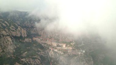 Montserrat Manastırı. İHA görüntüsü. İnsansız hava aracı bulutların altından manastıra doğru uçuyor. Görkemli hava yolculuğu: bulutlardan yükselen Montserrat Manastırı 'nın insansız hava aracı görüntüsü